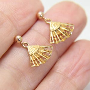 May include: A pair of gold-colored fan-shaped earrings. Each earring features a small, round stud and a delicate, openwork fan design. The earrings are made of a shiny, metallic material.