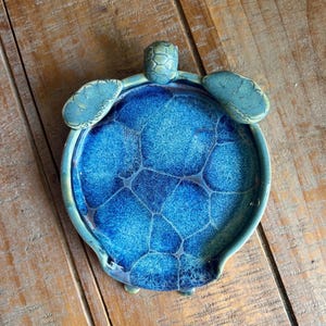 May include: A blue and green ceramic turtle dish with a textured shell design. The dish is perfect for holding jewelry, keys, or other small items.