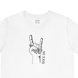 Puede incluir: Camiseta blanca con una ilustración en blanco y negro de una mano haciendo el gesto de rock and roll. El texto "ROCK ON" está escrito verticalmente debajo de la mano.