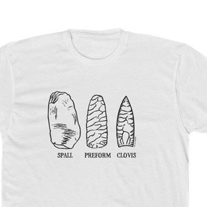 May include: White t-shirt with a black line drawing of three different types of stone tools. The tools are labeled "Spall", "Preform", and "Clovis".