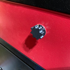 May include: A black star-shaped knob with a textured surface. The knob is attached to a red drawer.