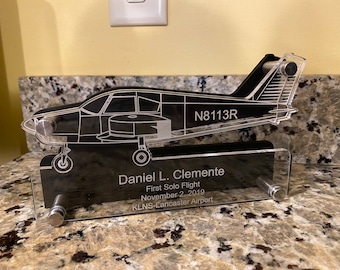 May include: A black acrylic plaque with a silver outline of a small airplane. The plaque reads "N8113R", "Daniel L. Clemente", "First Solo Flight", "November 2, 2019", and "KLNS-Lancaster Airport".