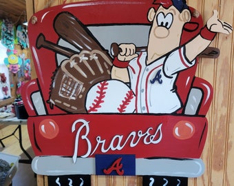 Puede incluir: Una camioneta roja con un jugador de béisbol de dibujos animados en la caja. El jugador lleva una camiseta blanca con una "A" roja en el frente y una gorra de béisbol azul. La camioneta tiene la palabra "Braves" escrita en la parte trasera y una "A" azul en el portón trasero. La camioneta está decorada con bates de béisbol, un guante y una pelota de béisbol.