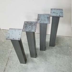 May include: Four metal table legs with square plates. The legs are different heights, ranging from about 15 inches to 20 inches.