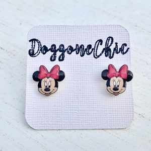Puede incluir: Un par de pendientes de bot&oacute;n de Minnie Mouse en una tarjeta blanca con el texto "Doggone Chic". Los pendientes son negros con un lazo rojo y una cara blanca.
