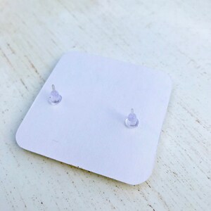 Puede incluir: Una tarjeta blanca con dos respaldos de pendientes de pl&aacute;stico transparente.