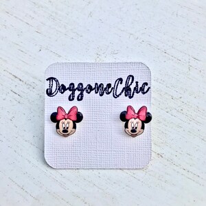 Puede incluir: Un par de pendientes de bot&oacute;n de Minnie Mouse con un lazo rosa en una tarjeta blanca con el texto "Doggone Chic".