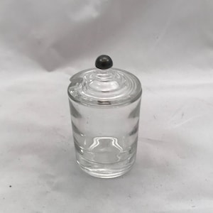 May include: A clear glass jar with a lid. The lid has a small, round knob on top.