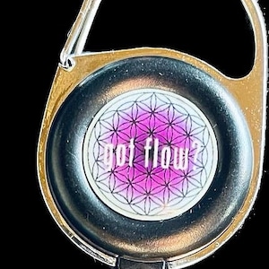 May include: A black retractable badge holder with a silver clip and a round, black, and silver disc with a pink and white geometric design and the text "got flow?"