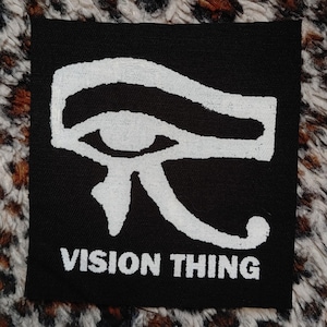 May include: Black fabric patch with a white stylised eye of Horus symbol and the text "VISION THING" below it.