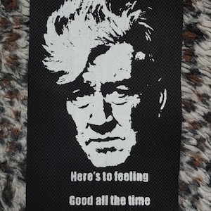 Op de afbeelding: Zwart-witte strijkpatch met een silhouet van een mannengezicht en de tekst "Here's to feeling good all the time".