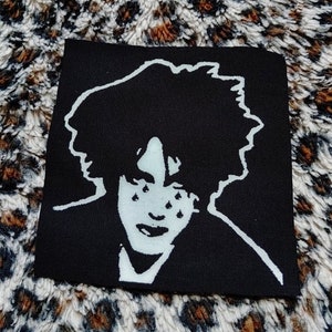 Op de afbeelding: Zwart-witte strijkpatch met een gestileerd portret van een persoon met donker haar en een witte omtrek. De ogen van de persoon zijn gesloten en ze huilt.