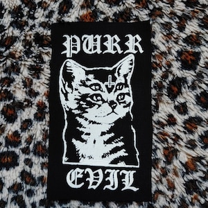 Peut inclure: Patch thermocollant noir et blanc avec une illustration de chat et le texte "PURR EVIL" en police gothique.