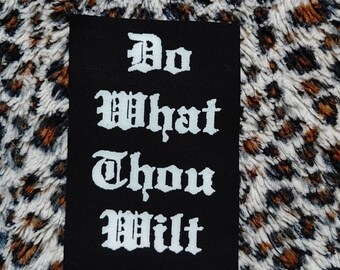 Könnte beinhalten: Schwarzer Patch mit weißem Text in alter englischer Schrift, der "Do What Thou Wilt" lautet.
