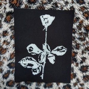 Op de afbeelding: Een zwarte stoffen patch met een witte roos en bladeren.