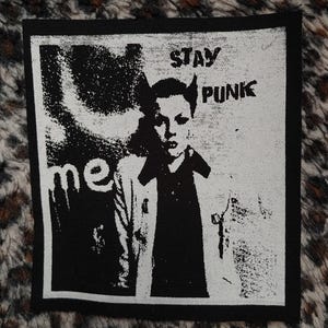 May include: Black and white patch with the text "Stay Punk" and a black and white image of two people. The person on the right is wearing a black jacket.