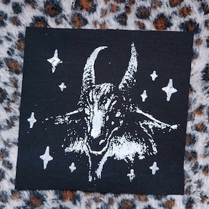May include: White iron-on patch with a black and white image of a goat's head with horns and stars around it. The patch is on a black fabric background.