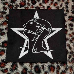 May include: Black embroidered patch with a white star and a stylized human head inside the star.