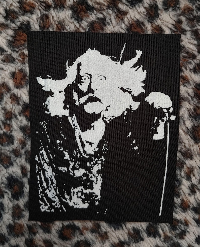 Peut inclure: Patch thermocollant noir et blanc repr&eacute;sentant la silhouette d'un homme avec de longs cheveux et une barbe, tenant un microphone. Le patch est con&ccedil;u pour &ecirc;tre cousu sur des v&ecirc;tements ou des sacs.