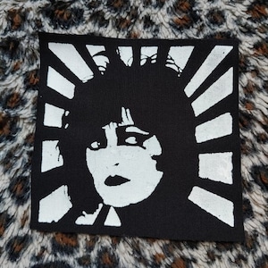 Może przedstawiać: Czarno-biała naszywka do prasowania z  stylizowanym portretem kobiety na białym tle i czarno-białym wzorem promieni słońca.