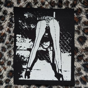 May include: Black and white patch featuring a stylized illustration of a person bent over. The figure is depicted in white against a black background, with a chain-link fence visible.