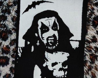 Könnte beinhalten: Schwarz-weiß gestickter Patch mit einer Kapuzenfigur, die einen Schädel in der Hand hält. Die Figur hat einen bedrohlichen Ausdruck und trägt einen gehörnten Helm. Der Patch ist auf schwarzem Hintergrund.