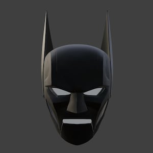 May include: A black mask with pointed ears and white eye openings. The mask has a geometric design and a prominent nose and mouth area, reminiscent of a superhero's cowl. The mask is set against a grey background.