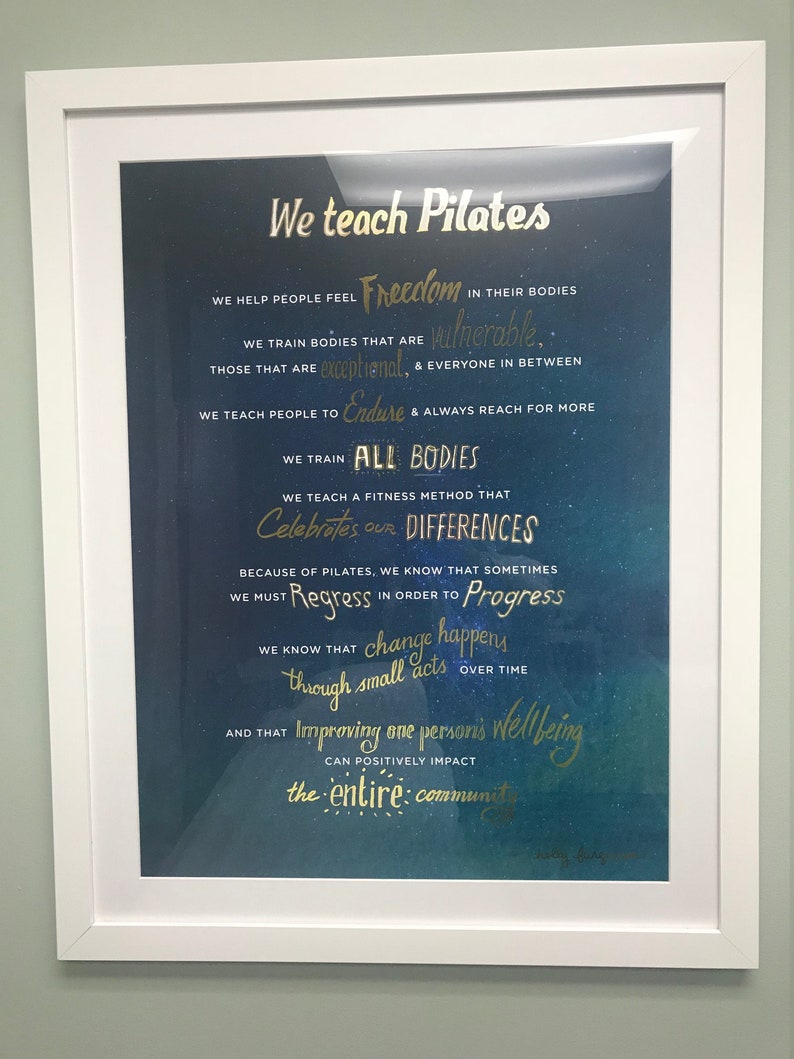 Peut inclure: Une affiche de motivation encadr&eacute;e avec un fond bleu et du texte dor&eacute;. Le texte dit "We teach Pilates" et comprend une citation sur l'aide aux gens &agrave; se sentir libres dans leur corps et &agrave; c&eacute;l&eacute;brer les diff&eacute;rences.