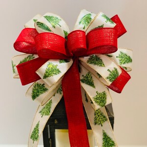 May include: A red and white Christmas bow with a green tree pattern on the white ribbon. The bow is tied around a black lantern.