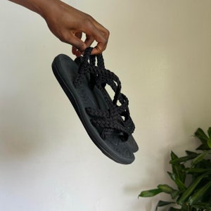 May include: Black rope sandals with a thick black sole. The sandals are tied up the ankle and have a criss-cross design.