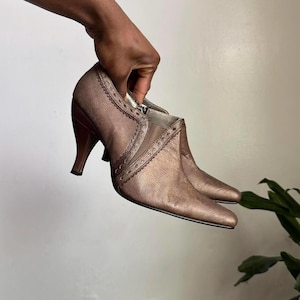 以下が含まれることがあります： ポインテッドトゥとハイヒールが特徴のブロンズカラーのアンクルブーツ。ブーツはテクスチャード加工が施されており、側面に装飾的なステッチが施されています。ヒールは約7.6cmです。