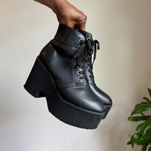 May include: A pair of black ankle boots featuring a high platform wedge sole, a rounded toe, and a lace-up front closure with silver-toned metal eyelets. The boots are constructed with a smooth matte finish and include black laces tied at the top.