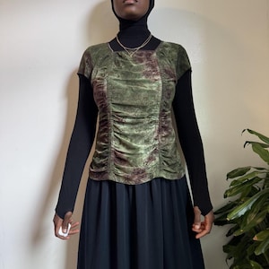 May include: A short-sleeved top featuring a square neckline and a green and brown floral pattern. The garment has a ruched front panel with vertical detailing, layered over a solid black long-sleeved base layer and a black skirt.
