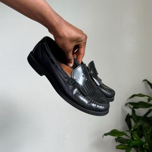 May include: Black leather tassel loafers with a brown leather insole.