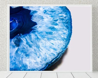 May include: Close-up of a blue and white agate slice with a white background. The agate has a natural, organic pattern with a deep blue center and white, crystalline edges.