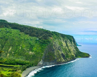 May include: A scenic coastal landscape featuring a lush green cliffside meeting the deep blue ocean under a cloudy sky. The image captures a view of the coastline with a black sand beach and foamy waves.