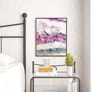 May include: A bedroom interior with a metal bed frame, white bedding, and a nightstand with a book, a small plant, and a decorative mug. A framed abstract painting with purple, pink, and blue hues hangs on the wall.