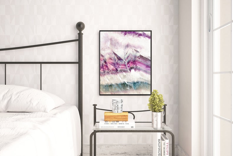 May include: A bedroom interior with a metal bed frame, white bedding, and a nightstand with a book, a small plant, and a decorative mug. A framed abstract painting with purple, pink, and blue hues hangs on the wall.