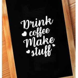 May include: A black chalkboard with a white wooden frame. The chalkboard has white text that reads "Drink coffee make stuff" with a small heart symbol before the words "coffee" and "stuff".