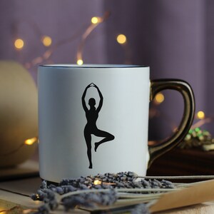 Peut inclure: Une tasse en c&eacute;ramique blanche avec une silhouette noire d'une personne en position de yoga. La tasse a une poign&eacute;e dor&eacute;e.