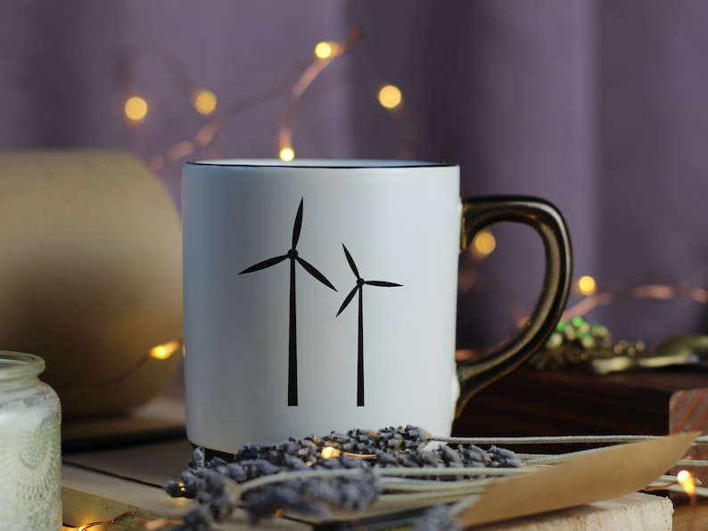 Puede incluir: Taza de cer&aacute;mica blanca con un contorno negro y una silueta negra de dos aerogeneradores. La taza tiene un asa dorada.