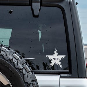 May include: A white star-shaped sticker with the word "VIP" inside, on the rear window of a black car.