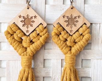 Op de afbeelding: Een paar gele kwast oorbellen met een houten hanger met een zon en sterren ontwerp.