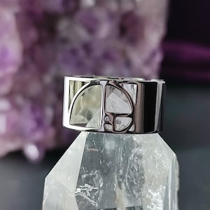 Può includere: Un anello d'argento con un designo di cristallo trasparente. L'anello è posto su un cristallo di quarzo trasparente.