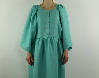 Puede incluir: Un vestido de lino turquesa con cuello redondo y mangas largas. El vestido tiene un frente abotonado y una falda fruncida.