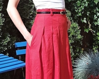 May include: A vibrant red skirt with a high waist and pleats, paired with a black belt. The skirt is knee-length and appears to be made of a lightweight fabric. The model is wearing a white top. The skirt has pockets.