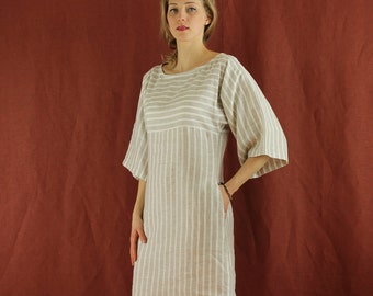 Puede incluir: Un vestido de lino a rayas beige y blanco con cuello de barco y mangas 3/4. El vestido tiene un corte holgado y una silueta recta.