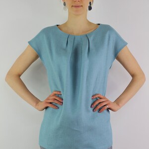 May include: A light blue linen top with a gathered neckline and short sleeves. The top is loose fitting and has a relaxed silhouette.