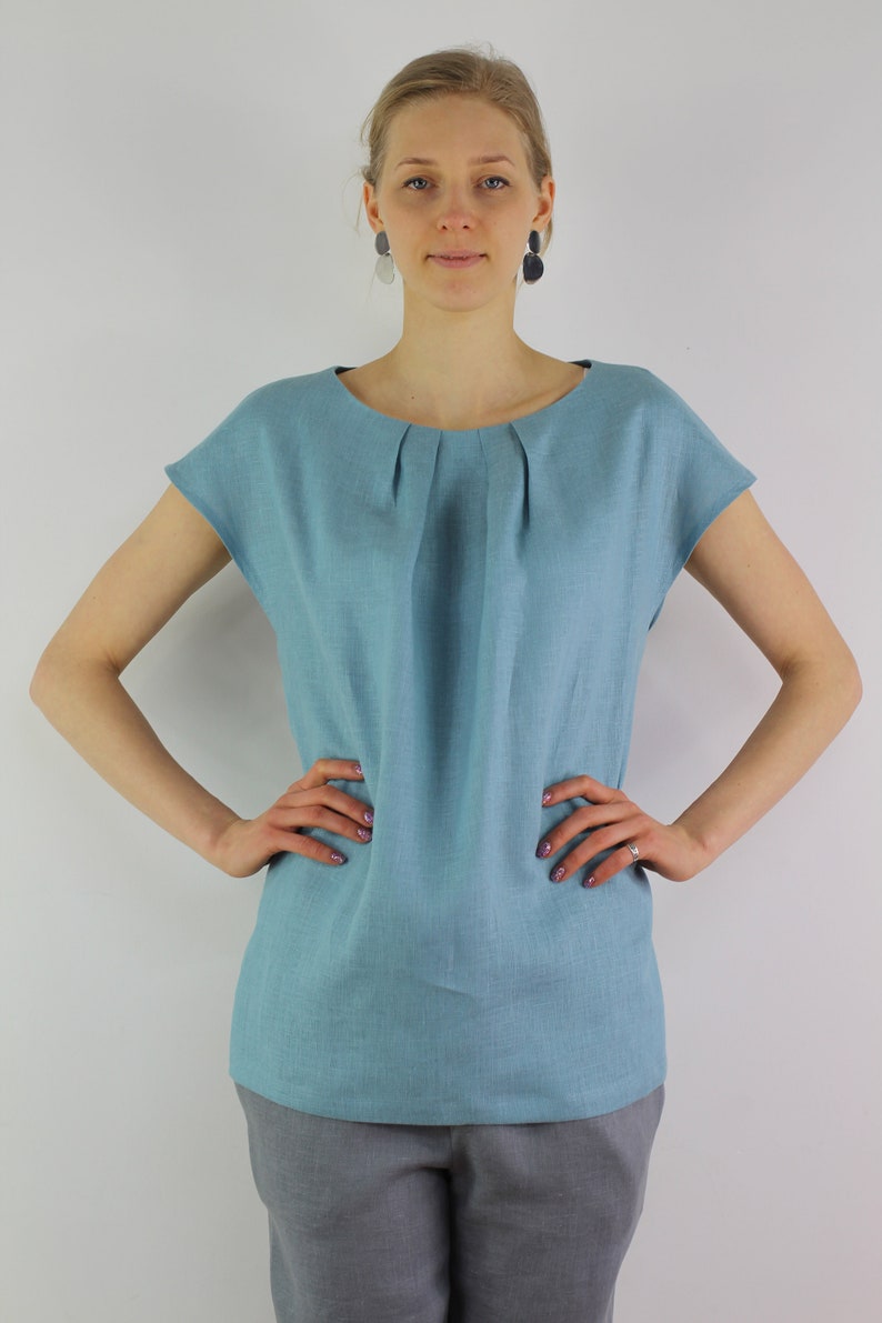 May include: A light blue linen top with a gathered neckline and short sleeves. The top is loose fitting and has a relaxed silhouette.