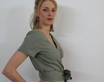 May include: A sage green wrap top with short sleeves and a tie at the waist. The top is made of a soft, linen-like fabric.